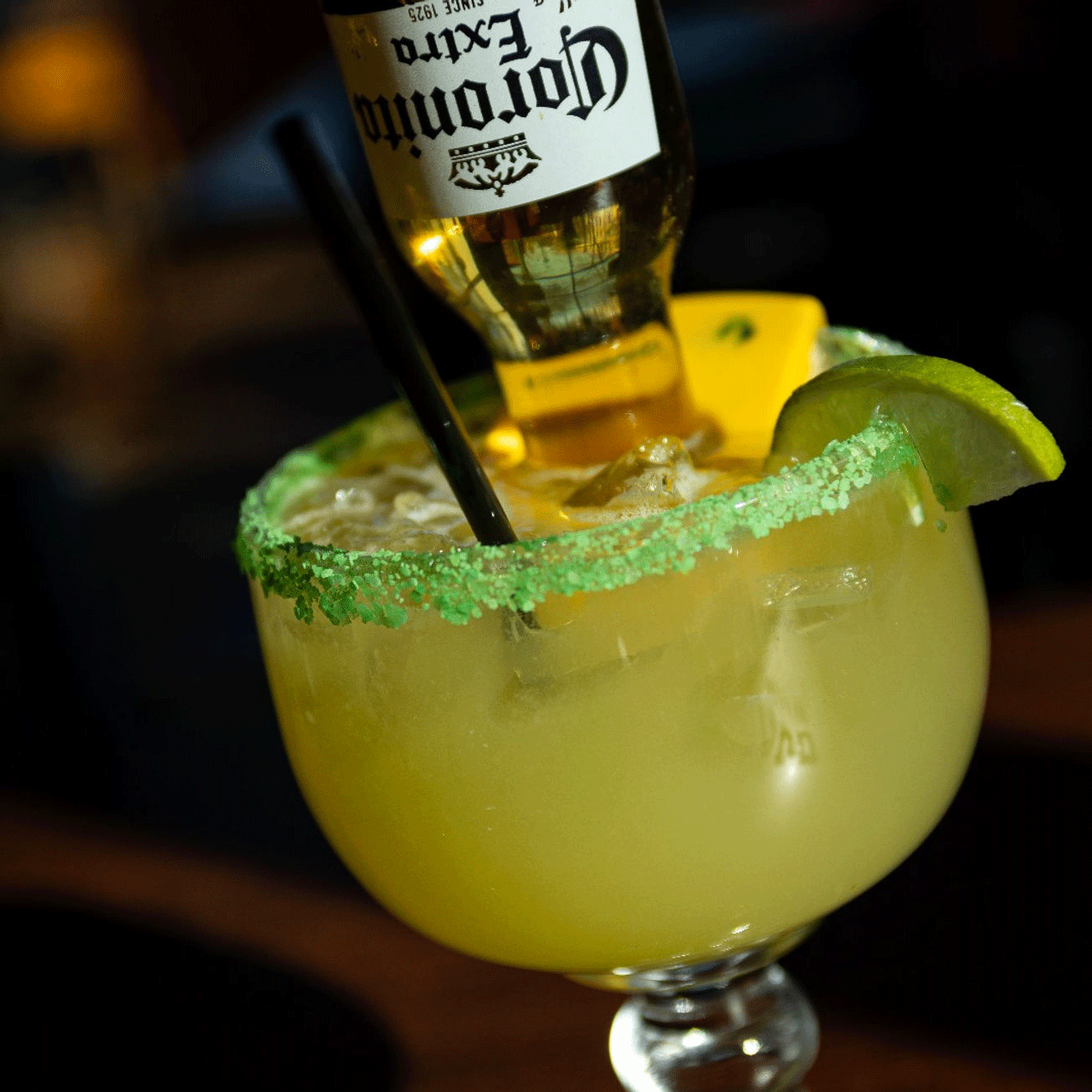 Margarita cocktail with a Corona bottle upside down in it, lime wedge and green salt rim.