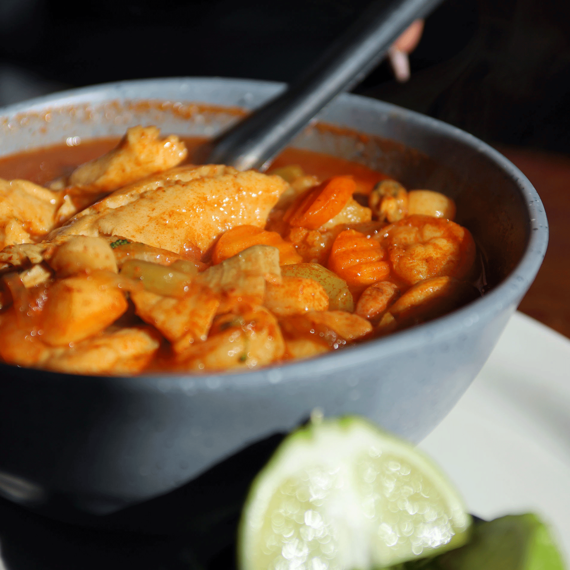 Bowl of stew with chicken, carrots, and chickpeas; lime wedge in foreground.