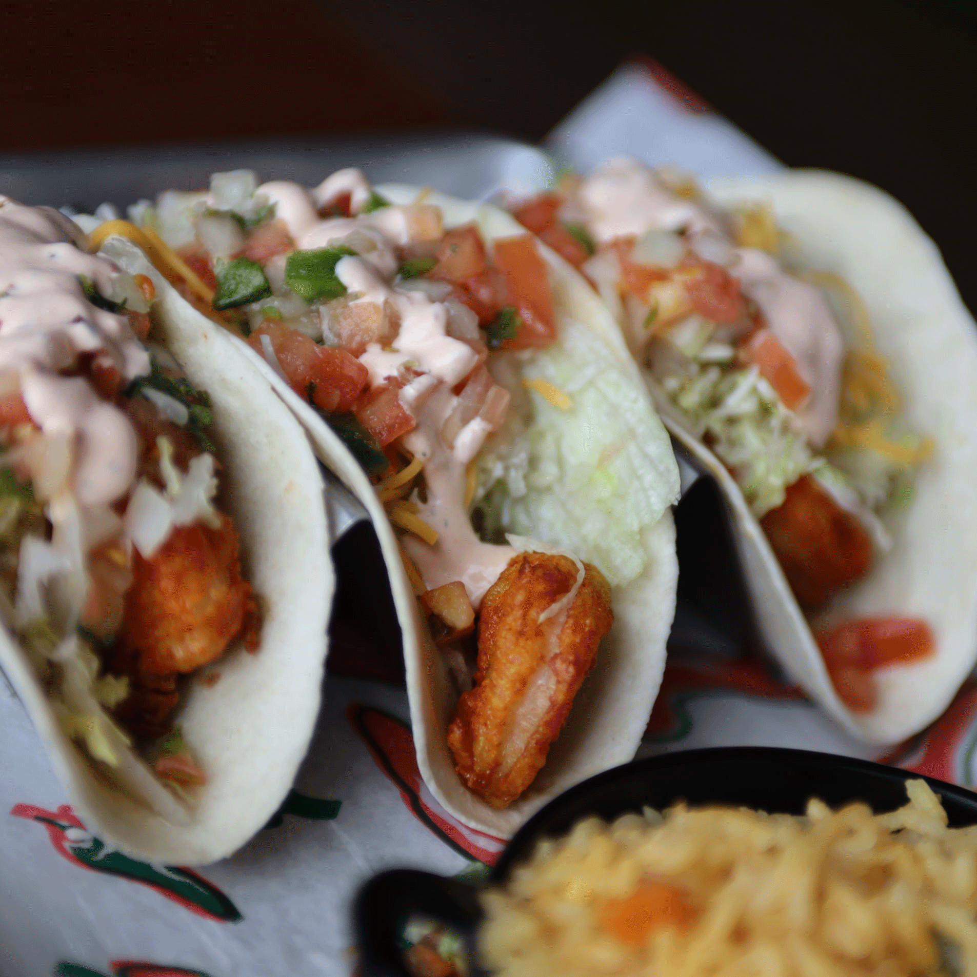 Three fish tacos in soft shells with toppings and sauce, with rice in a bowl.