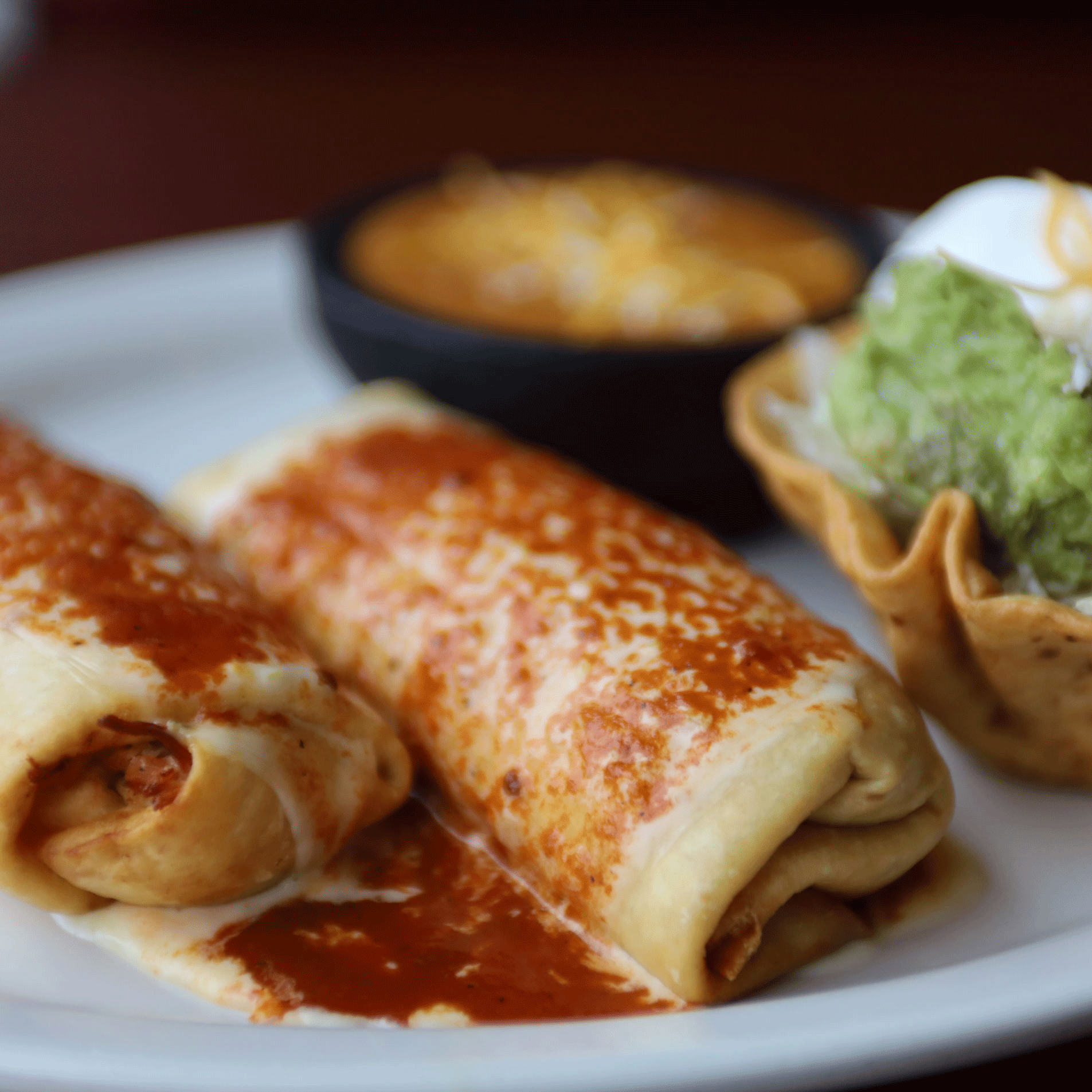 Two enchiladas with red sauce, guacamole in a taco shell, and cheesy dip.