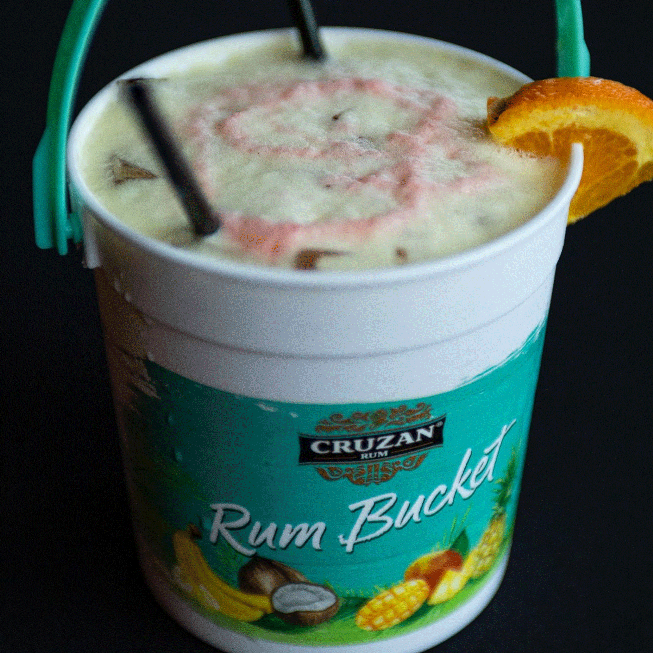 Rum Bucket cocktail in a white plastic bucket, orange slice garnish, straws.