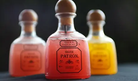 Three Patron tequila bottles with colorful drinks inside, against a dark background.