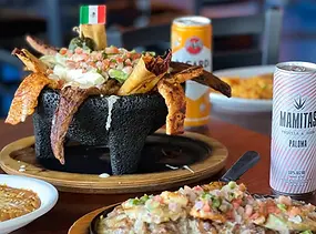 A dish of nachos in a black bowl, with drinks and salsa.