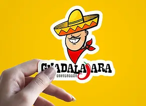 Hand holding a Guadalajara restaurant sticker featuring a smiling cartoon man in a sombrero and red scarf.