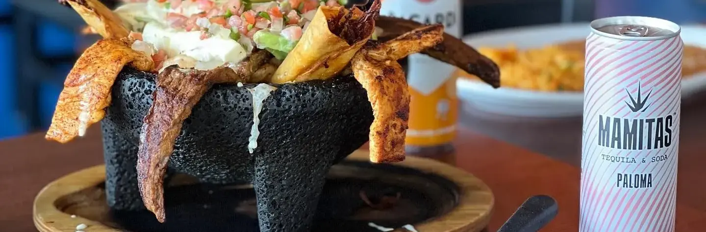A molcajete bowl filled with food and an unopened can of Mamitas hard seltzer.