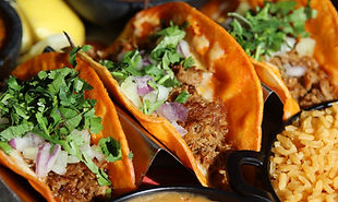 Close-up of tacos in orange shells, filled with meat, onions, and cilantro, served with rice.