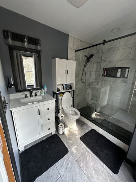 Modern bathroom with black-and-white decor, glass shower, vanity, and toilet on gray tile floor