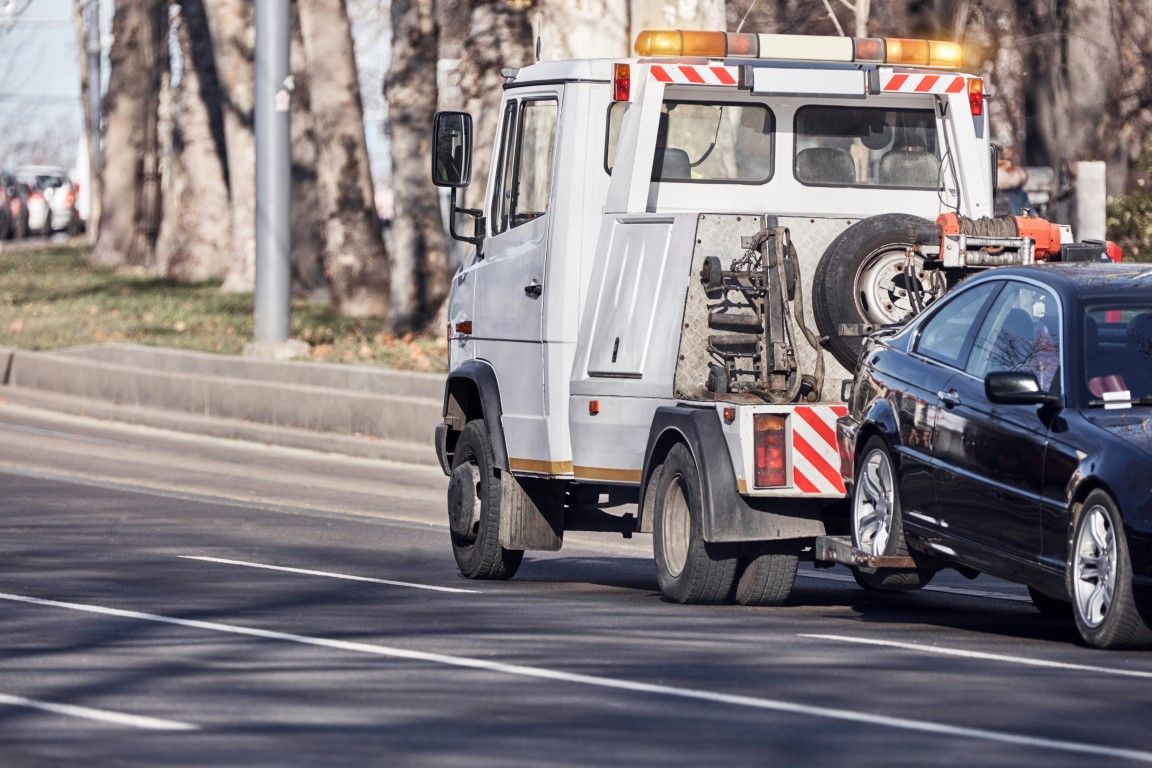 Tow truck towing a black car on a road, both vehicles are white and black.
