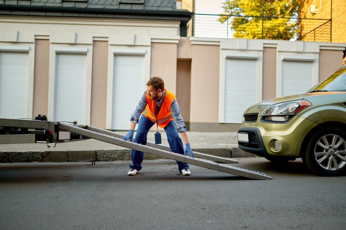 Man in orange vest, loading car onto a tow truck with a ramp in a residential street.