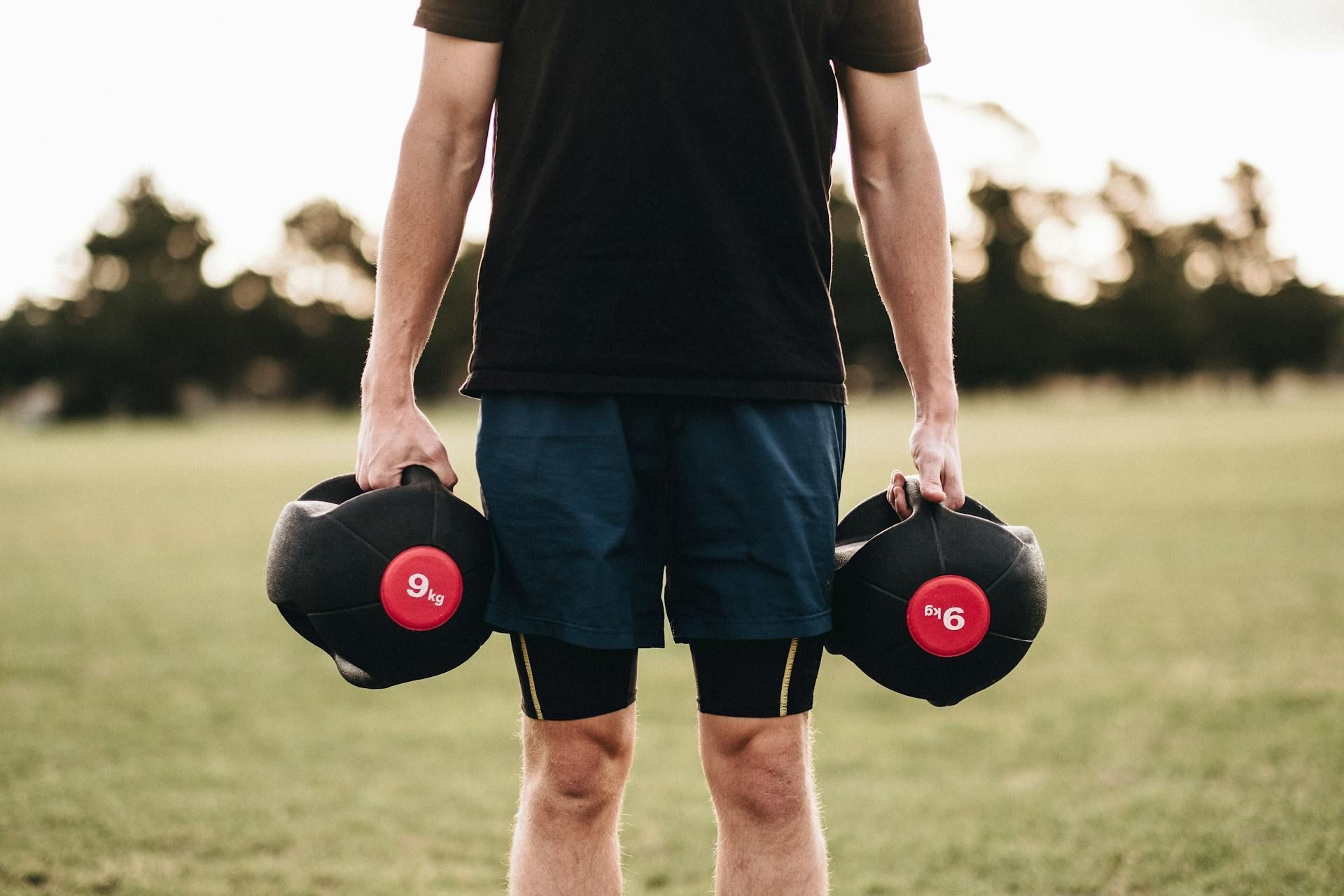 Turning Weakness Into Strength A man is holding two dumbbells in his hands in a field.