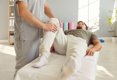 Physical therapist assisting a man on step platforms in a bright rehab room