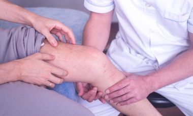 Physical therapist assisting a seated patient with leg stretches on a treatment table in a clinic