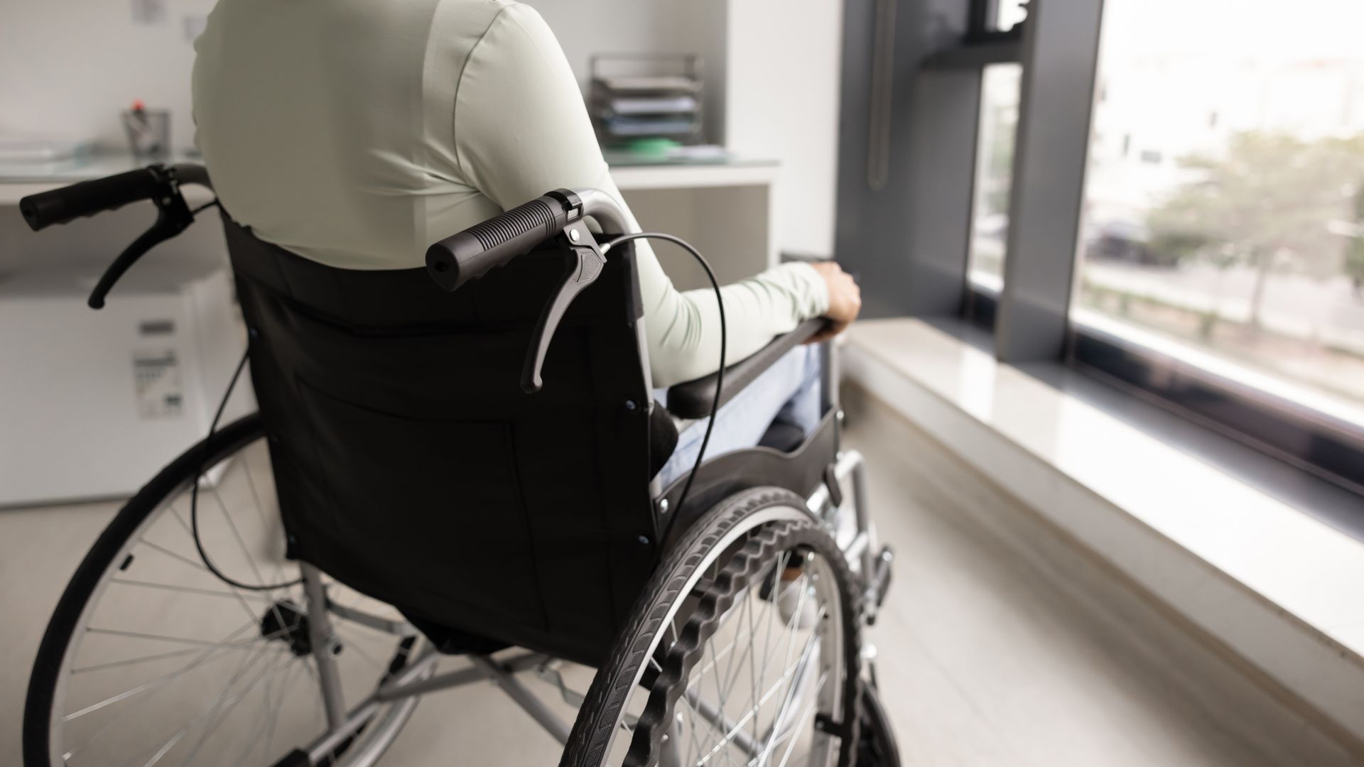 Person in a black wheelchair near a bright window in a room.