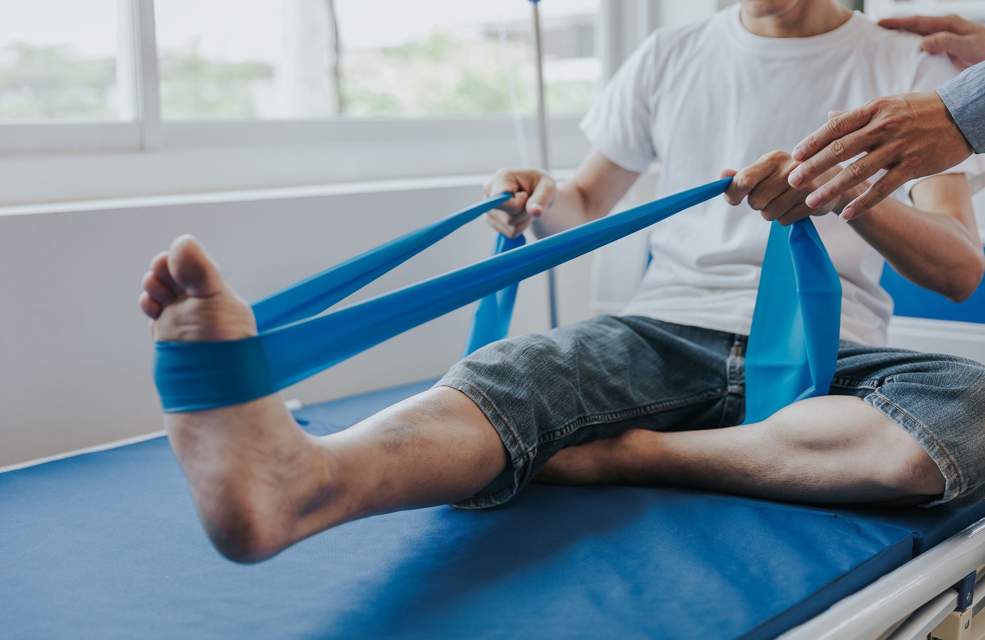 Person stretching a leg with a blue resistance band on a therapy table.