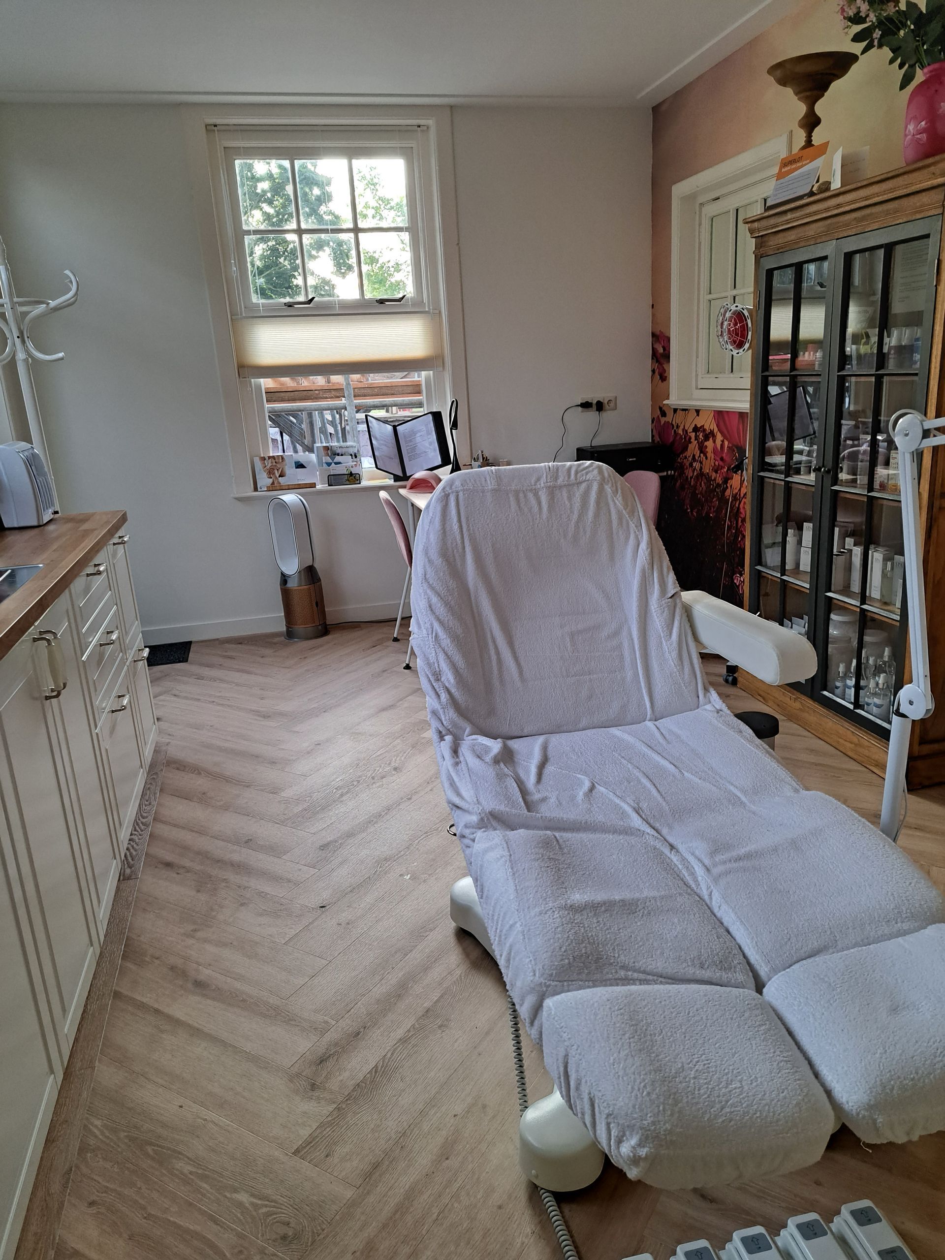 Lichte woonkamer met een witte relaxfauteuil, een glazen kast en een raam aan de achterkant.