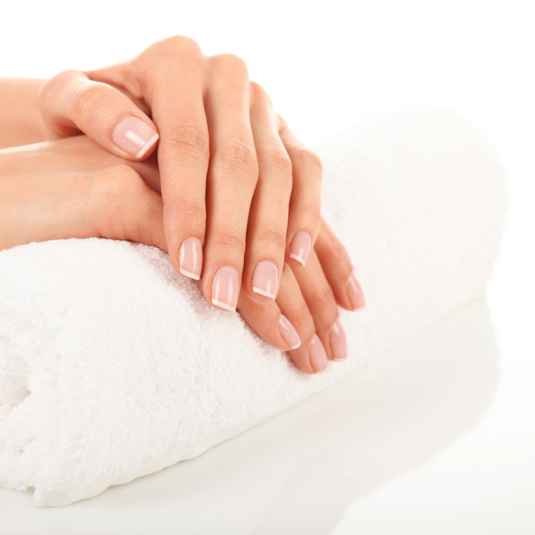 Verzorgde handen rusten op een opgerolde witte handdoek in een spa-omgeving.