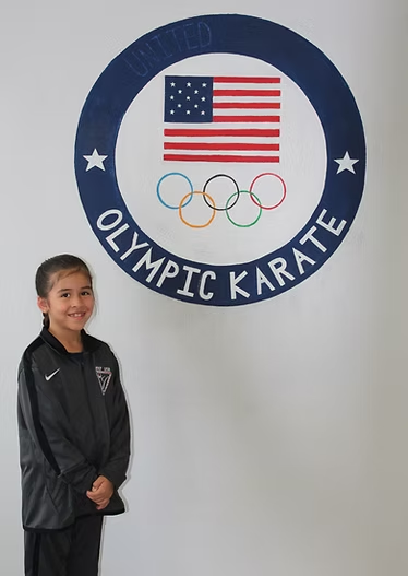 A young girl stands in front of an olympic karate logo
