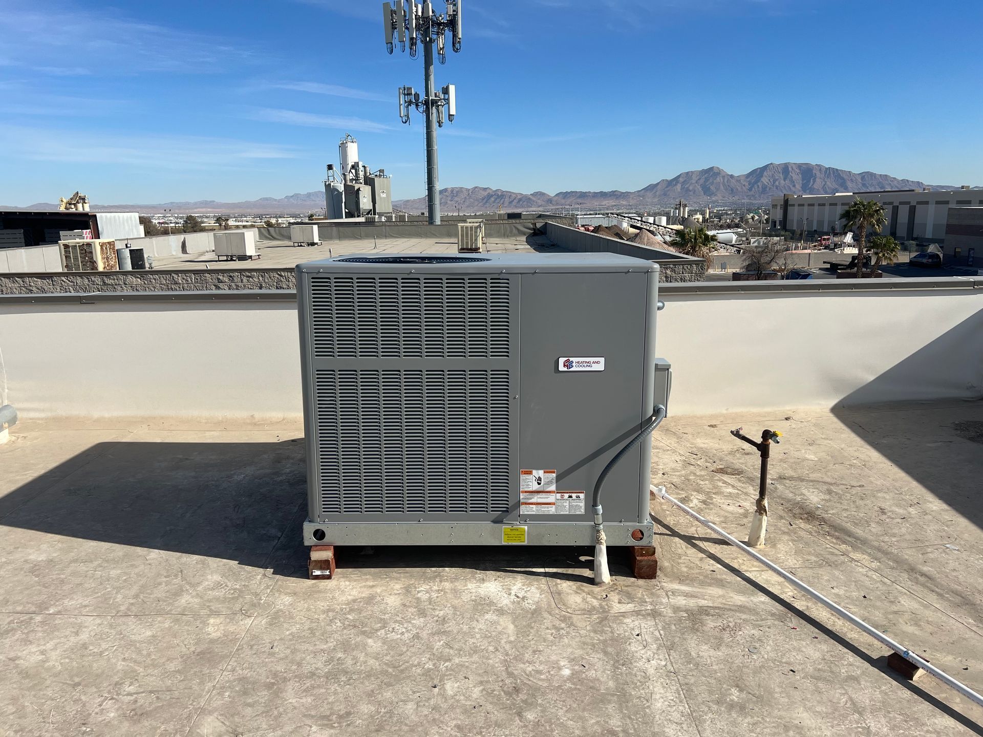 Gray rooftop HVAC unit on a flat roof with city buildings and mountains in the background.