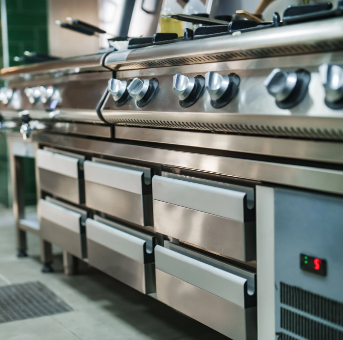 Stainless steel commercial oven with multiple control knobs and pull-out drawers in a kitchen