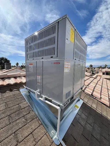 Outdoor rooftop HVAC unit mounted on metal supports against a blue sky and tiled roof