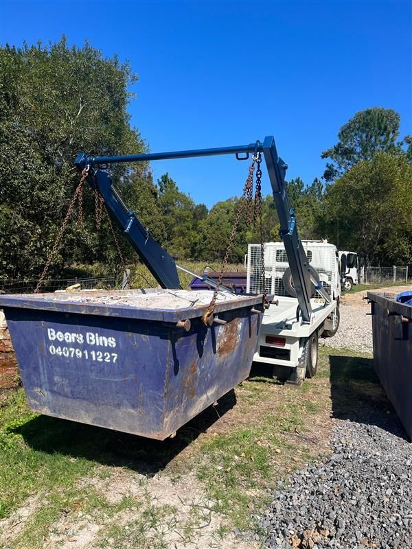 Blue skip bin being lifted by a truck with a crane against a backdrop of trees and a blue sky — Bears Bins Skip Hire In Meridan Plains, QLD