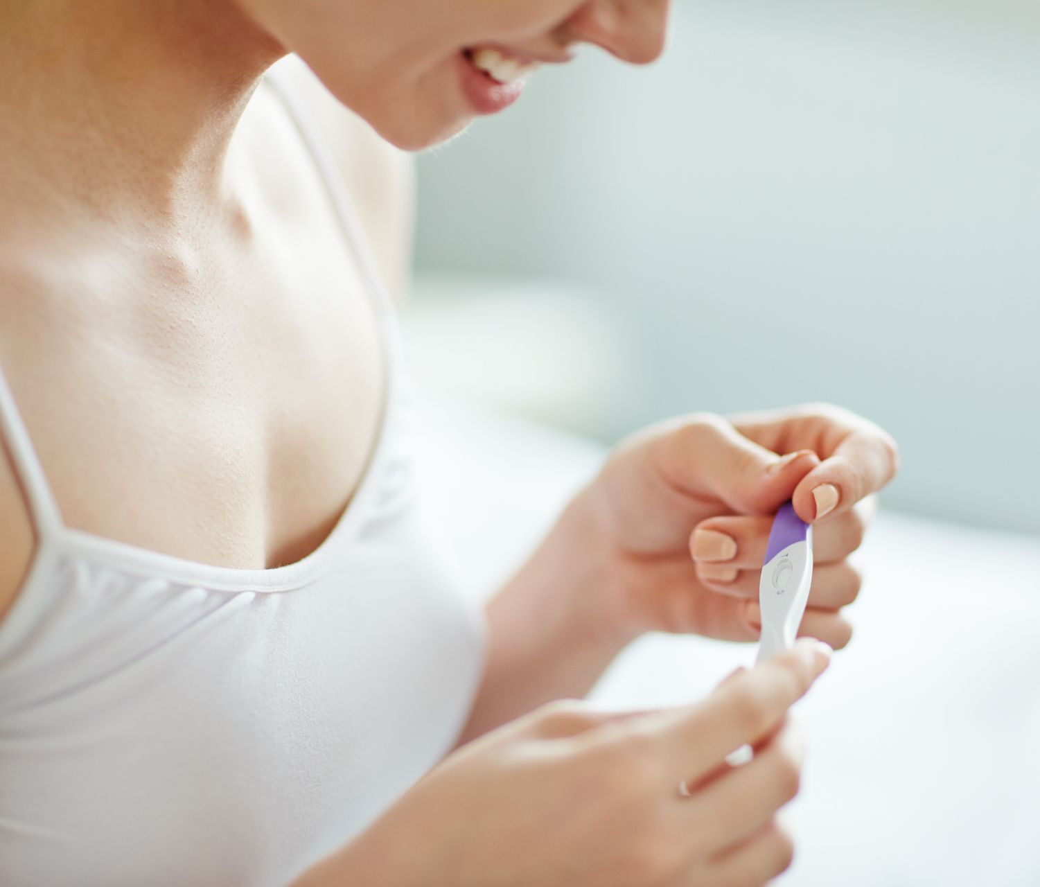 artistic shot of the same woman, she is still smiling, looking down at the positive pregnancy test, she has been successful after a visit to a holistic fertility center near vernon hills