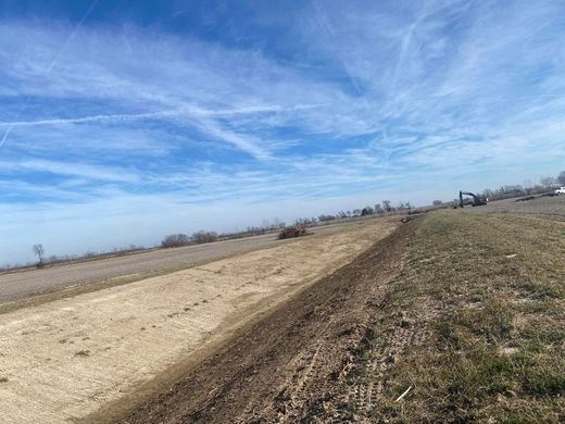 Dirt road beside a grassy field under a blue, partly cloudy sky.
