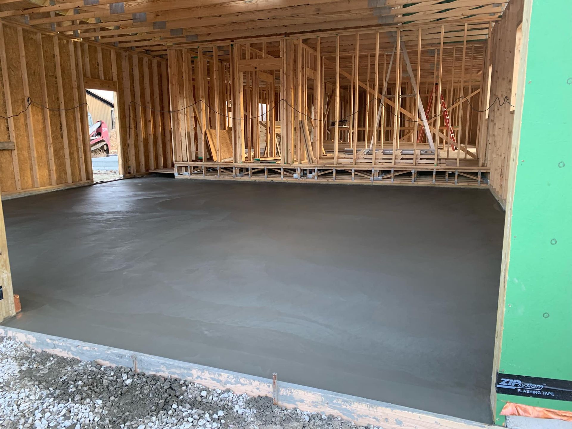 Interior of a framed house under construction with a smooth gray concrete floor and exposed wooden studs.