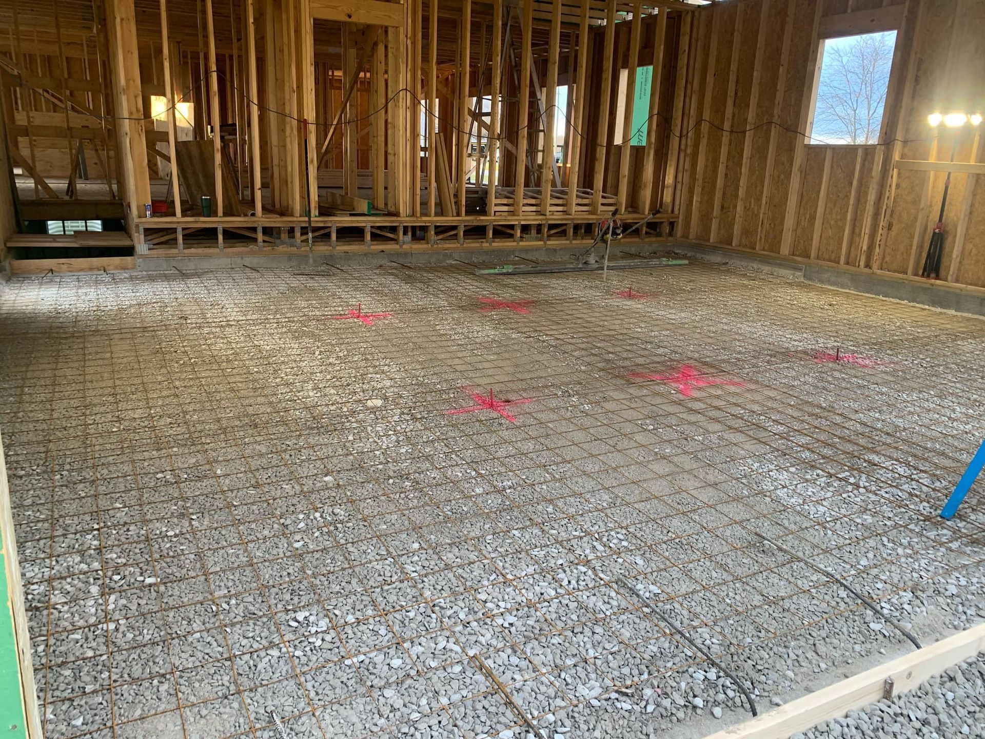 Framed house interior with exposed wooden walls and a concrete slab floor marked for construction.