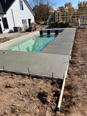 Rectangular backyard swimming pool with a gray concrete deck beside a white house and mulch border