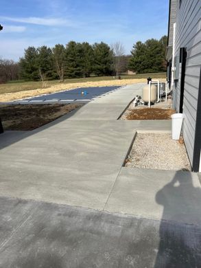 Concrete walkway beside a house with gravel, landscaping, and a backyard pool under construction