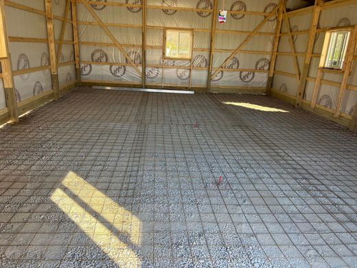Empty unfinished room with exposed wall framing and wire mesh floor, sunlight streaming through windows.