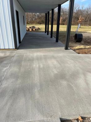 Covered concrete walkway beside a white building with black posts and a yard beyond.