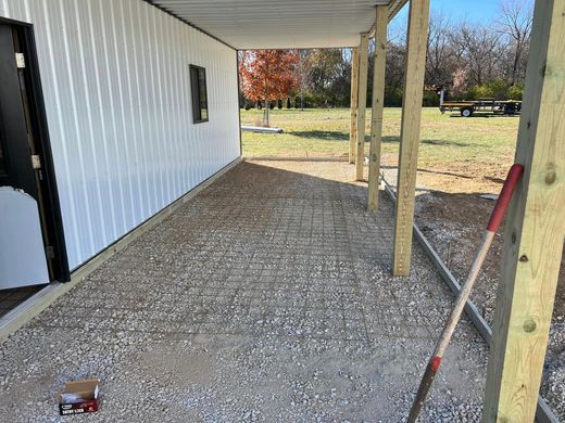 Covered gravel walkway beside a white building with wooden posts and a yard beyond