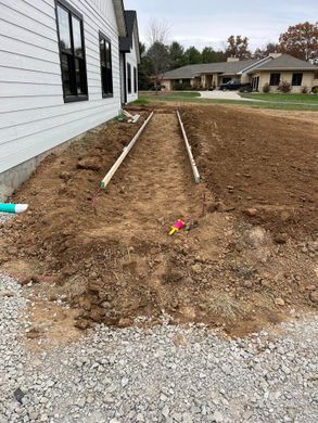 Dirt trench beside a white house, with two white pipes running through a gravel yard.