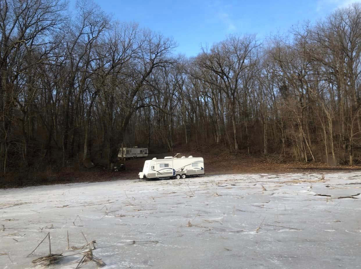 Abandoned white RV in a snowy, leafless wooded clearing