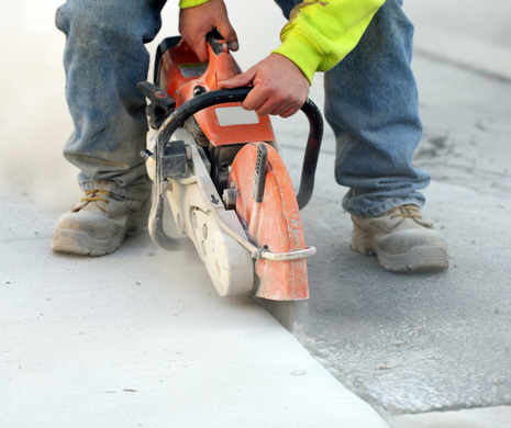 Worker using an orange concrete saw to cut a white concrete slab outdoors