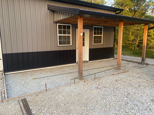 Gray building with dark trim and a small wooden porch over a gravel area