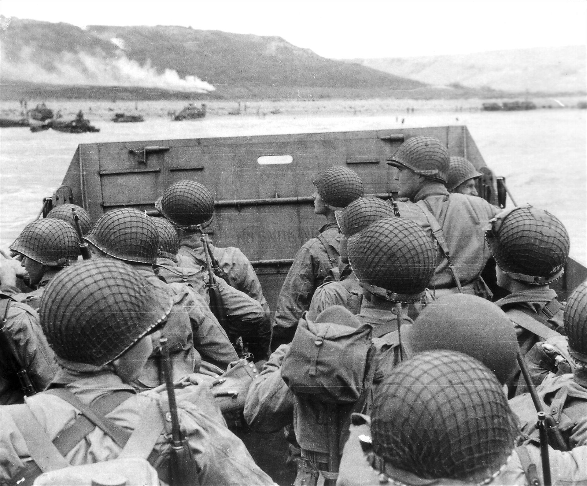 A vintage black-and-white photo of US veterans on the ground, looking forward while handling a rifle.