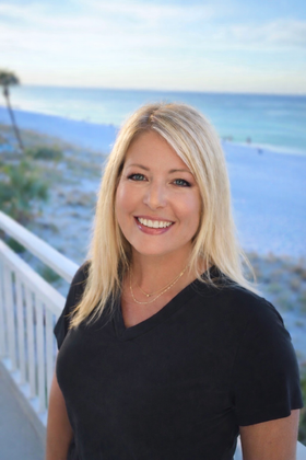 Cindi standing by a white railing with a beach and ocean in the background