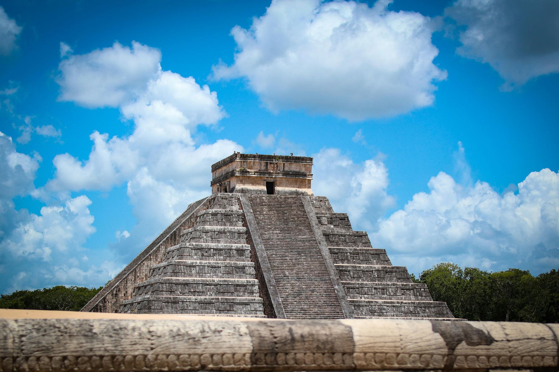 Mayan pyramid temple against a bright blue sky with scattered clouds
