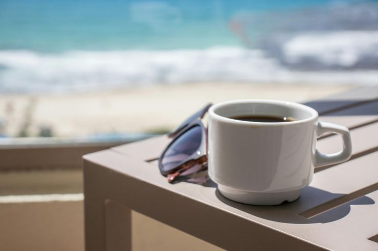 White coffee cup and sunglasses on a table with a blurred beach view in the background