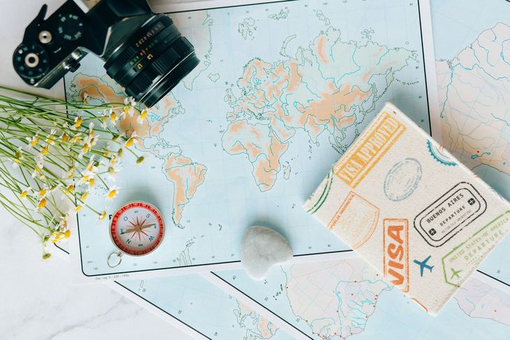 Travel flat lay with passport, camera, compass, and map on a light background