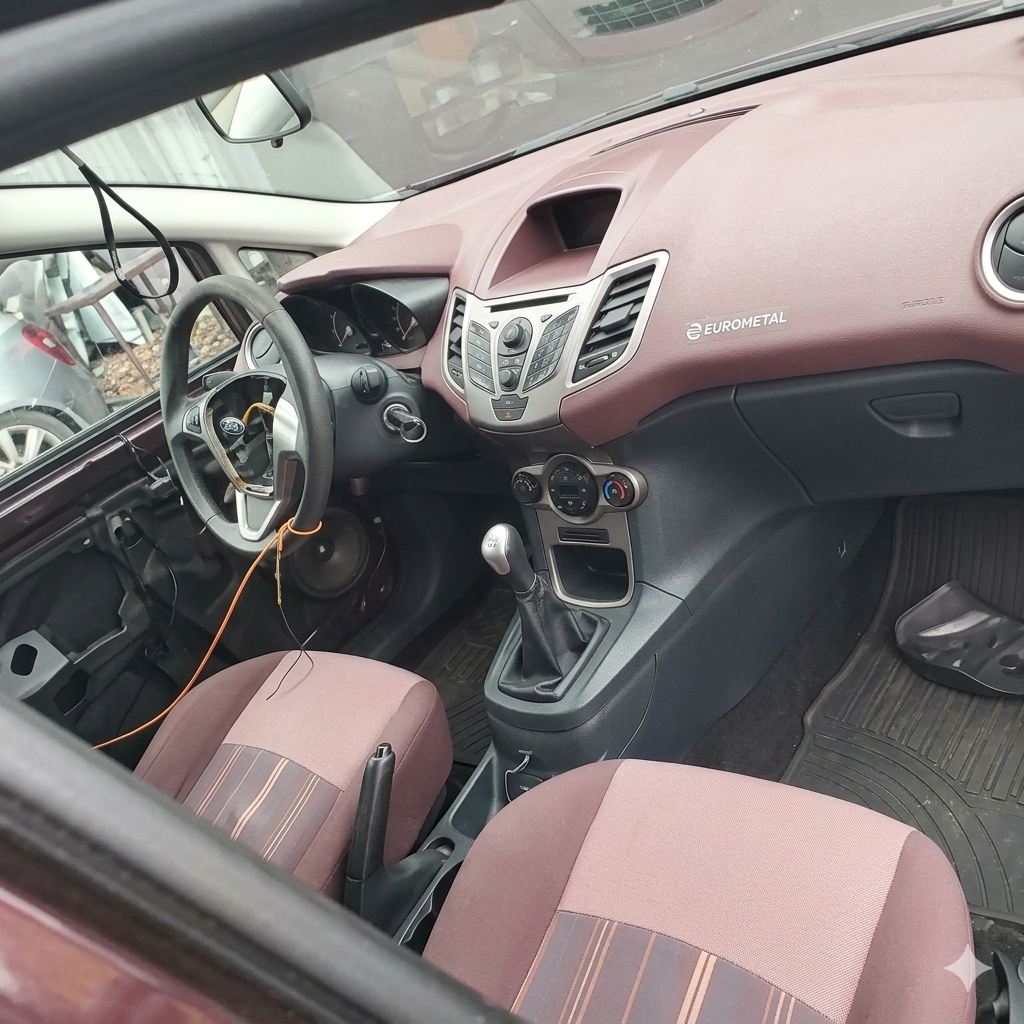 Vista interna di un'auto bordeaux e grigia, che mostra il cruscotto, il volante e i sedili in tessuto.