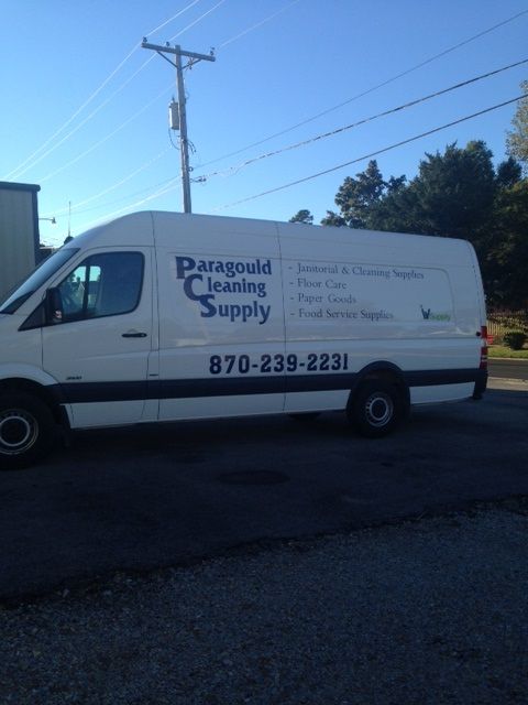 A white Paragould Cleaning Supply delivery van parked on an asphalt lot under a blue sky.