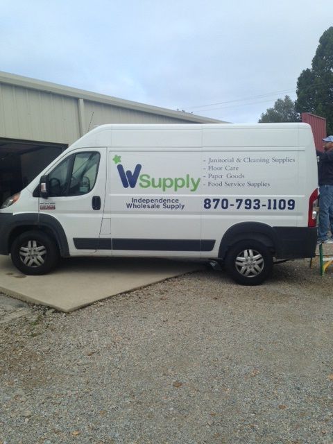 A white Independence Wholesale Supply van parked outdoors, displaying the company logo and contact number on the side.