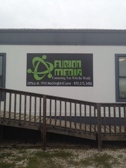 A sign for Fusion Media featuring a green atom logo and contact information mounted on a building wall above a ramp.