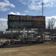 A billboard for NEA Turf Care with their phone number against a backdrop of a clear sky and a utility truck below.