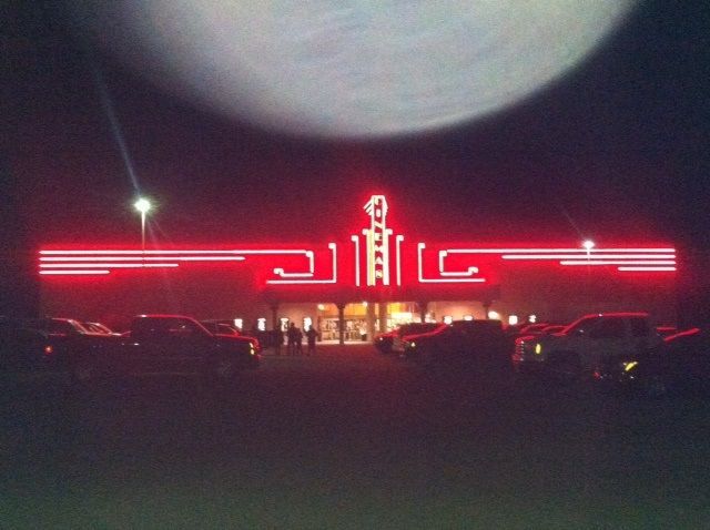 A neon-lit building with Art Deco style architecture at night, featuring glowing red lines and a parking lot out front.