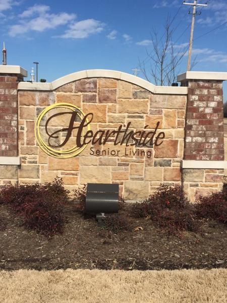 Stone entrance sign for Hearthside Senior Living, featuring gold lettering on a tan stone wall with brick columns.